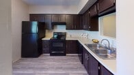 Located at 99 Turtle Creek Dr. in Asheville, NC, this two-floor residence offers a functional and comfortable layout spread across multiple levels. The kitchen is a standout feature, outfitted with rich dark cabinetry, light countertops, black appliances including a refrigerator and electric range, a double stainless steel sink, and durable wood-look flooring — providing ample storage and a practical workspace. An open pass-through connects the kitchen to the living and dining area, which transitions from hardwood-style flooring to plush carpet and features a sliding glass door that invites natural light and outdoor access. The carpeted bedrooms are generously sized, each offering closet storage and windows with blinds for natural light and privacy. One bedroom includes a walk-in closet with built-in shelving. The bathrooms are well-equipped: one features a white vanity with a single sink, brushed nickel fixtures, and a lighted mirror, while another includes dark cabinetry, a light stone-tone countertop, and a tub-shower combination. Throughout, the interior maintains a neutral warm palette with beige walls, white trim, and textured ceilings, creating a clean, move-in-ready ambiance suited to a variety of lifestyles.
