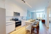 Located at 101 SW 1st St in Dania Beach, Florida, this well-appointed one-bedroom, one-bathroom residence offers a thoughtfully designed open-concept layout. Light hardwood flooring flows throughout, complementing the clean, modern aesthetic.

The kitchen and living area form the heart of the home, featuring high-gloss white cabinetry, white subway tile backsplash, stainless steel appliances including a side-by-side refrigerator, electric range, built-in microwave, and dishwasher, all anchored by a matte black faucet. Track and pendant lighting illuminate the space, which opens directly to the living area accented by soft blue walls and large floor-to-ceiling windows leading to a private balcony with outdoor views.

The bedroom is comfortably scaled, finished with the same hardwood flooring and clean white walls, offering a calm and restful retreat. Three closets provide generous storage throughout the unit. A dedicated laundry area and utility room add everyday convenience.

The bathroom is a standout feature, showcasing marble-look tile on both the floors and shower walls, a frameless glass shower enclosure with matte black fixtures, a floating vanity, and an illuminated mirror. A light-filled hallway with louvered closet doors connects the living spaces to the private quarters, completing this modern coastal residence.
