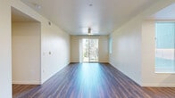 This thoughtfully designed single-floor residence offers three bedrooms, two bathrooms, a living room, and a kitchen within a compact and efficiently utilized floor plan. The galley-style kitchen is outfitted with stainless steel appliances — including a refrigerator, electric range, built-in microwave, and dishwasher — paired with navy blue lower cabinetry, white upper cabinets extending to the ceiling, and light countertops. Recessed lighting and a window at the end of the kitchen bring in natural light and views of surrounding greenery. The living room is bright and open, featuring rich wood-style plank flooring, a ceiling fan, and a sliding glass door that opens to an outdoor balcony, framing lush tree views. The two secondary bedrooms are carpeted in soft grey and each feature windows with horizontal blinds overlooking the outdoors. The primary bedroom mirrors the living area with wood-style flooring, a ceiling fan, and its own sliding glass door with balcony access. Both bathrooms feature blue accent cabinetry with white countertop sinks, clean white walls, and distinctive blue flooring. One bathroom includes a full tub and shower combination. The hallways connect spaces seamlessly, maintaining a clean and modern aesthetic throughout.