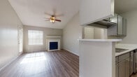 This single-story residence offers a thoughtfully laid-out floor plan with a bright, open feel throughout. The living area is a standout space, showcasing soaring vaulted ceilings that amplify the sense of openness, a ceiling fan with integrated lighting, and a classic fireplace framed by a white mantle with a deep blue tile surround. Large windows with horizontal blinds invite abundant natural light, while durable hardwood-style flooring flows seamlessly through the main living areas and bedrooms.

The kitchen is designed for practicality and efficiency, featuring gray cabinetry, light stone-look countertops, and a suite of black and stainless steel appliances including a gas range and refrigerator. A half-wall peninsula connects the kitchen to the living space, creating a natural pass-through and social flow.

The bedrooms are generously proportioned, each equipped with a ceiling fan and windows that allow natural light to filter in. One bedroom includes access to a walk-in closet with built-in shelving. The bathroom features a gray vanity with stone-look countertops, a single basin sink, and mirrored cabinetry for added storage. Textured ceilings are present throughout, complementing the home's neutral gray and white color scheme for a clean, move-in ready aesthetic.