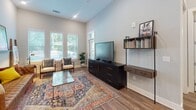 This thoughtfully designed single-floor residence in Morrisville, NC offers a contemporary open-concept layout with high-end finishes throughout. The kitchen is a standout feature, boasting two-tone cabinetry with white upper and gray lower cabinets, a geometric tile backsplash, stainless steel appliances, and a large center island with a built-in sink and quartz countertops. Elegant glass pendant lights hang above the island, adding a refined touch. Rich wood-look flooring runs continuously throughout the space, creating a warm and cohesive aesthetic.

The living area impresses with notably tall ceilings and large windows that invite an abundance of natural light and offer views of the surrounding greenery. The open floor plan allows the kitchen and living room to flow seamlessly together, maximizing the sense of space.

The bedroom features a bold deep teal accent wall that adds character and contrast, complemented by a large window with outdoor views. An en-suite bathroom includes a glass-enclosed walk-in shower with tile surround, a dual-sink white vanity with quartz countertops, a framed mirror, and wood-look flooring, delivering a clean and modern finish throughout.