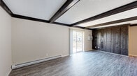 Located at 3406 Queensway Dr in Erlanger, Kentucky, this single-floor residence offers a thoughtfully arranged layout with a variety of distinct living spaces. The living room serves as the architectural centerpiece of the home, showcasing bold dark-stained exposed ceiling beams that contrast sharply against the textured white ceiling. Grey wood-look vinyl flooring runs throughout this area, and a striking accent wall of dark vertical wood paneling adds a rustic, layered character. Sliding glass doors open directly onto a private deck, filling the space with natural light and providing seamless outdoor access.

The galley-style kitchen is efficiently designed with white cabinetry lining both sides, granite-look countertops, stainless steel appliances including a refrigerator and dishwasher, and durable light wood-look flooring. A closet at the far end adds practical storage.

The bedrooms are carpeted and bright, each featuring windows that bring in natural light and baseboard heating. The neutral tones create a calm, restful atmosphere throughout.

Two full bathrooms serve the home, both finished with white vanity cabinetry, large mirrors with lighted fixtures, and wood-look flooring. One bathroom includes a tub-shower combination, while the other features a streamlined layout. The overall aesthetic is clean and functional throughout.