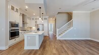Located at 17014 Fairmount Way in Charlotte, NC, this two-story home offers a thoughtfully designed layout with quality finishes throughout. The main level centers around an open-concept kitchen and dining area, where rich hardwood-style flooring flows seamlessly underfoot. The kitchen is a standout, outfitted with crisp white shaker cabinetry extending to the ceiling, a large center island with a white quartz countertop and undermount sink, stainless steel appliances including a gas cooktop, double wall ovens, built-in microwave, and French door refrigerator, plus a wall-mounted range hood. Pendant lighting and recessed fixtures illuminate the space, while crown molding adds a refined touch. A staircase with white balusters connects the main level to the upper floor. The upper level features generously sized bedrooms with plush carpeting, large windows providing ample natural light, and ceiling fans. The bathrooms are finished with marble-style tile flooring, white vanities, and framed mirrors; one features a glass-enclosed walk-in shower, while another offers a tiled tub-shower combination. A dedicated laundry room houses a full-size Whirlpool front-load washer and dryer, completing this well-equipped home.
