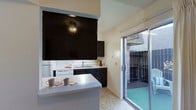 This two-story residence offers a practical and well-organized layout designed for comfortable everyday living. The kitchen is a standout feature, showcasing dark cabinetry that extends to the upper portion of the wall, creating a bold contrast against the light-colored walls and white countertops. A peninsula-style breakfast bar provides additional workspace and casual dining space, complete with seating. The kitchen is equipped with white appliances, including a refrigerator and dishwasher, and features a double-basin sink positioned beneath cabinetry for convenient storage. A sliding glass door in the kitchen fills the space with natural light and provides seamless access to a private enclosed patio, which is framed by a brick wall and offers a compact outdoor retreat. The vaulted ceiling detail visible near the kitchen adds a sense of openness and vertical dimension to the space. Light-toned flooring throughout complements the neutral walls, contributing to a bright and airy atmosphere. The two-floor configuration of the home provides a natural separation between living and private spaces, making it a well-structured and versatile residence suitable for a range of lifestyles.