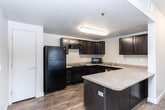 Located in Magna, Utah, this single-story, one-bedroom, one-bathroom unit offers a well-organized layout designed for comfortable, efficient living. The combined kitchen and living area forms the heart of the home, where rich hardwood-style flooring flows throughout. The living room features a ceiling fan with light fixture, textured ceiling, and a sliding glass door with vertical blinds that allows natural light to fill the space. A secondary window provides additional brightness to the adjacent dining or entry area.

The kitchen is a standout, outfitted with dark espresso cabinetry, granite-style countertops, a peninsula for additional prep space, and black appliances including a refrigerator, range, and built-in microwave. The hardwood-style flooring continues seamlessly from the living area into the kitchen.

The bedroom is a comfortable, well-proportioned room with soft carpet flooring and a built-in overhead shelf, offering practical storage options. The full bathroom is ADA-accessible, featuring grab bars at the bathtub and toilet, an open under-sink vanity with granite-style countertop, a combined tub and shower, and wood-look tile flooring. The dedicated laundry room includes a full-size washer and dryer with built-in wire shelving for added storage convenience.