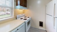Located at 45 East St in Victor, NY, this two-floor residence offers a straightforward and functional layout spread across two levels. The kitchen is designed as a galley-style space, featuring rich dark wood cabinetry on both sides, white appliances including a coil-burner electric range and full-size refrigerator, light-toned countertops, and updated wood-look vinyl plank flooring. An under-cabinet range hood and a wall-mounted heating unit contribute to the kitchen's practical setup, while a textured ceiling adds a classic touch overhead.

The living areas on the upper level are carpeted in neutral tones and benefit from natural light through windows that overlook the surrounding greenery. A prominent staircase with a black metal railing connects the two floors and serves as a visual focal point. The open layout of the upper level allows for flexible use of space, with baseboard heating units present throughout. Bedrooms are carpeted and bright, each with access to additional rooms or hallways, and feature windows that bring in natural light.

The bathroom is clean and simply appointed, with tile flooring, a bathtub with surround, a toilet, and chrome fixtures including a towel bar and toilet paper holder. Overall, the space presents a practical and livable environment in a quiet Victor, NY setting.
