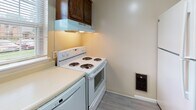 Located at 45 East St in Victor, NY, this two-floor residence offers a straightforward and functional layout spread across two levels. The kitchen is designed as a galley-style space, featuring rich dark wood cabinetry on both sides, white appliances including a coil-burner electric range and full-size refrigerator, light-toned countertops, and updated wood-look vinyl plank flooring. An under-cabinet range hood and a wall-mounted heating unit contribute to the kitchen's practical setup, while a textured ceiling adds a classic touch overhead.

The living areas on the upper level are carpeted in neutral tones and benefit from natural light through windows that overlook the surrounding greenery. A prominent staircase with a black metal railing connects the two floors and serves as a visual focal point. The open layout of the upper level allows for flexible use of space, with baseboard heating units present throughout. Bedrooms are carpeted and bright, each with access to additional rooms or hallways, and feature windows that bring in natural light.

The bathroom is clean and simply appointed, with tile flooring, a bathtub with surround, a toilet, and chrome fixtures including a towel bar and toilet paper holder. Overall, the space presents a practical and livable environment in a quiet Victor, NY setting.