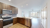Located in Olathe, Kansas, this well-appointed 3-bedroom, 2-bathroom residence offers a thoughtfully designed single-floor layout. The open-concept kitchen and living area serves as the heart of the home, showcasing rich dark walnut cabinetry, a quartz waterfall-edge island with an undermount sink, stainless steel appliances including a French door refrigerator and electric range, and a textured tile backsplash. Light hardwood flooring runs throughout the main living areas, complementing the bright, airy atmosphere created by large windows and recessed lighting. The living room features a ceiling fan and expansive windows that frame serene views of the landscaped grounds and community green spaces. The generously sized primary bedroom includes plush carpeting, a ceiling fan, and abundant natural light. It is paired with a spacious walk-in closet outfitted with multi-tiered shelving and hanging rods. The primary bathroom impresses with a dual-sink vanity topped with quartz counters, dark wood cabinetry, and a glass-enclosed walk-in shower with tile surround. Additional bedrooms offer carpeted floors and large windows with scenic outdoor views, providing comfortable and versatile spaces throughout.