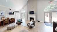 Located at 2200 University Suites Drive in Greenville, NC, this single-floor community clubhouse offers a well-appointed and versatile space designed to serve residents across a range of needs. The entry foyer makes an immediate impression with soaring vaulted ceilings, a signature arched transom window above double glass doors, and light hardwood flooring that carries throughout the main areas. Natural light flows generously through multiple windows, creating a bright and open atmosphere. A welcoming reception desk greets visitors near the entrance, while an adjacent private office features high ceilings, large windows, warm wood furnishings, and ample workspace. The two living areas provide comfortable lounge seating, dining tables, and tasteful coastal-inspired décor, including framed artwork and decorative mirrors, offering residents inviting spaces to gather or relax. The kitchen is outfitted with white cabinetry, granite countertops, stainless steel appliances including a full-size refrigerator and microwave, and a deep utility sink. Vending machines and a coffee station provide added convenience. The dedicated fitness center is generously sized, featuring multiple treadmills, ellipticals, a stationary bike, cable weight machines, free weights, wall mirrors, and a large ceiling fan — all set on durable rubberized flooring beneath bright skylight panels.