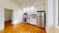 Situated in the heart of Richmond, Virginia, this single-floor unit at 909 E Main St offers a well-designed layout that balances comfort and functionality. Rich, warm-toned hardwood floors run throughout the living areas and bedrooms, lending the space a classic charm that complements its clean, white walls and high ceilings that create an open, airy atmosphere.

The kitchen is a standout feature, outfitted with crisp white shaker cabinetry, a neutral tile backsplash, and a full suite of stainless steel appliances including a range, microwave, dishwasher, and refrigerator. A large window in the kitchen invites ample natural light and offers views of the surrounding urban streetscape.

The bedroom areas are bright and generously proportioned, with soaring ceilings and closet space for storage. Frosted glass interior doors add a contemporary touch while allowing light to flow throughout the space. The bathroom is finished with tasteful, modern details including a granite-topped dark wood vanity, tile flooring, and a full tub-shower combination with clean white subway tile surround and brushed nickel fixtures.

Ceiling fans provide added comfort, and the overall design maintains a neutral, move-in-ready palette. This unit offers a refined urban living experience in one of Richmond's central downtown corridors.