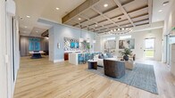 Located on Dynamic Boulevard in Wesley Chapel, FL, this single-floor community amenity space offers a generously sized, open-concept layout designed for both relaxation and social gatherings. The interior is defined by soaring coffered ceilings with warm wood-toned beams and recessed lighting, lending an air of architectural sophistication throughout.

The main lounge area features light hardwood flooring, a large sectional seating arrangement, and a statement circular chandelier with globe accents. Adjacent to the lounge is a bar counter clad in turquoise tile with bar stool seating, a mosaic tile accent wall, and pendant lighting, creating an inviting focal point. A long marble-topped island provides additional seating and gathering space.

A dedicated games room offers a full-size billiards table, blue velvet barrel chairs arranged on a checkerboard tile floor, and coastal pelican artwork, complemented by natural light from large windows with sheer drapery. A separate seating nook with built-in display shelving and a wall-mounted TV provides a more intimate lounge setting.

Glass-partitioned walls enclose a private meeting or office area, while large French doors open to an outdoor terrace with exterior views. The cohesive coastal color palette of soft blues, whites, and natural wood tones creates a bright, welcoming ambiance throughout the space.