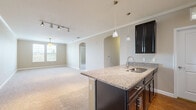 This single-floor residence offers a well-designed open-concept layout that seamlessly connects the kitchen and living areas. The kitchen serves as a central focal point, showcasing dark espresso cabinetry paired with light granite countertops on a peninsula island equipped with a stainless steel sink. Pendant lighting hangs above the island, complementing track lighting overhead. Stainless steel appliances, including a refrigerator, range, and microwave, complete the kitchen's functional and polished aesthetic. Crown molding and wood-look flooring add refinement to this space.

The open living area flows naturally from the kitchen, featuring plush carpeting, neutral-toned walls, and arched architectural doorways that add character. Natural light enters through multiple windows. The bedrooms continue the warm, neutral palette with soft carpet flooring, ceiling fans, and window blinds. One bedroom benefits from a spacious walk-in closet outfitted with wire shelving on both sides, offering generous storage capacity.

The bathroom features a full tub-shower combination with built-in shelving, wood-look tile flooring, and granite-topped dark vanity cabinetry, maintaining the cohesive design found throughout the residence.