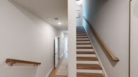This well-appointed three-story home offers a functional and modern layout across three distinct levels. The ground floor houses an attached garage with a polished concrete floor, automatic opener, and interior access — providing convenient storage and utility space. The main living level features an open living room filled with natural light from large windows, complemented by a ceiling fan and hardwood-style flooring. The adjacent kitchen is outfitted with gray shaker cabinetry, light quartz countertops, an undermount sink, and recessed lighting, creating a clean and contemporary workspace. A hallway bathroom and dedicated office with a window and closet access round out this floor. The upper level is home to two comfortable bedrooms, each featuring plush carpet, ceiling fans, and generous natural light. The primary bedroom includes its own closet, while a second closet serves additional storage needs. Two bathrooms on this floor include a full bath with a soaking tub and shower combo finished in crisp white. Throughout the home, neutral tones, clean white trim, and wood-toned stair railings with warm hardwood steps connect all three floors seamlessly, creating a cohesive and inviting aesthetic.