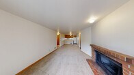 Located in University Place, WA, this two-bedroom, one-bathroom single-floor residence offers a functional and comfortable layout. The living room serves as the heart of the home, highlighted by a classic brick wood-burning fireplace and sliding glass doors that open onto a private balcony with outdoor views — filling the space with natural light and a welcoming ambiance. Ceiling fan lighting above connects the living area to the adjacent kitchen, which features warm oak cabinetry, white appliances including a refrigerator, dishwasher, and range, along with a stainless steel sink beneath a window. A peninsula counter separates the kitchen from the living area, adding definition to each space. Both bedrooms are carpeted and bright, with windows fitted with blinds that frame neighborhood views. The primary bedroom includes a wide sliding-door closet, providing ample storage. The second bedroom offers a similarly comfortable feel with generous proportions. A hallway connects the main areas and leads to the full bathroom, which includes a shower/tub combo with a frosted privacy window. Throughout the residence, neutral tones, wood-trimmed doors, and consistent flooring create a clean, cohesive aesthetic.