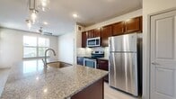 This thoughtfully designed 1-bedroom, 1-bathroom unit offers a functional and modern living experience across a single floor. The open-concept kitchen and living area serves as the heart of the home, highlighted by a large central island topped with granite countertops and a built-in sink, illuminated by three stylish pendant lights. Rich dark-wood cabinetry, a tile backsplash, and a full suite of stainless steel appliances—including a refrigerator, electric range, and microwave—complete the kitchen. Light wood-style flooring extends throughout the main living area, which features crown molding and a ceiling fan, and opens to a private exterior door with transom window, allowing ample natural light and outdoor access.

The bedroom is carpeted for comfort, features a ceiling fan, and receives natural light through a large window with outdoor views. An adjacent closet provides convenient storage. The bathroom is finished with tile flooring, a granite-topped dark vanity, and a full tub-shower combination. Crown molding and recessed lighting throughout the unit contribute to a clean, polished aesthetic, while neutral tones create a bright and welcoming atmosphere throughout.