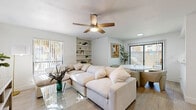 Located at 8330 N 19th Ave in Phoenix, AZ, this single-story 2-bedroom, 1-bathroom home offers a cohesive, light-filled interior with a clean, neutral palette throughout. The living room serves as the heart of the home, featuring light wood-style flooring, a ceiling fan, built-in shelving, and large windows with vertical blinds that invite an abundance of natural light. The open layout connects the living area to a dining space, creating a functional and welcoming atmosphere. The galley-style kitchen is efficiently designed with white cabinetry, ample counter space, a double sink, and full appliances — maximizing every inch of the space. The primary bedroom is a comfortable retreat with a ceiling fan, a window with outdoor views, and wood-style flooring consistent with the rest of the home. The second bedroom offers similar finishes with an arched mirror accent and ceiling fan, providing flexibility as a guest room or home office. The bathroom features a white vanity with stone-look countertops, a large mirror, and a tub-shower combination. A connecting hallway ties all rooms together seamlessly. Throughout the home, the bright whites and warm wood tones create a calm, airy ambiance well-suited to Phoenix living.