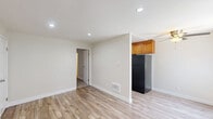 Located at 9035 Topanga Canyon Blvd in Los Angeles, CA, this single-floor unit offers a functional and efficiently designed layout. The open-plan living, dining, and kitchen area serves as the heart of the home, finished with light wood-style flooring that lends warmth and continuity throughout. The kitchen features warm-toned wood cabinetry positioned above a full-size refrigerator, providing practical storage solutions. Recessed lighting illuminates the main living area, while a ceiling fan and wall-mounted air conditioning unit ensure year-round comfort. A window with vertical blinds allows natural light to filter in, brightening the space. The bedroom is generously proportioned and features plush carpeting, a window with outdoor views, and access to a dedicated closet, offering ample storage. The bathroom is appointed with a warm wood vanity, granite countertops, a large mirror, and overhead lighting, creating a clean and functional space. Neutral, light-toned walls throughout the unit contribute to a bright and airy ambiance, making the space feel open and inviting. The unit also includes a private entry door, adding a sense of convenience and accessibility.
