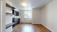 Located in the Phinney Ridge neighborhood of Seattle, Unit 35 at 3635 Phinney Ave N offers a thoughtfully designed single-floor studio layout that maximizes every inch of its space. Warm wood-look flooring runs continuously throughout, lending a cohesive and inviting feel to the entire unit.

The kitchenette is outfitted with sleek dark-toned cabinetry, stainless steel countertops, a single-basin sink, an overhead microwave, and a full-size refrigerator alongside open shelving for added storage. The clean, modern aesthetic carries into the main living area, which is bathed in natural light from a window with views of the surrounding neighborhood rooftops.

A built-in organizational station near the entry features open wall shelves, a hanging rod, and a fold-down desk surface — ideal for remote work or daily use. The electrical panel is neatly integrated into this entryway wall. The bathroom includes a walk-in shower stall finished in clean white tile with a built-in niche and chrome fixtures, maintaining the unit's minimalist design language.

The bright, neutral wall palette and efficient use of built-in features make this studio a functional and modern living space in one of Seattle's well-connected residential neighborhoods.