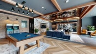 Located at 2135 Waterside Drive in Nashville, TN, this expansive amenity lounge is a thoughtfully designed social space that blends industrial character with contemporary sophistication. The open-plan layout is anchored by striking herringbone-patterned hardwood flooring that flows throughout, complemented by large-format slate tile in key areas.

The space is defined by its bold architectural details, including exposed wood beam ceilings painted in a rich slate blue-gray, dramatic halo ring pendant lighting, and exposed brick columns that add warmth and texture. A standout herringbone-patterned reclaimed wood accent wall serves as a focal point, framing a wall-mounted flat-screen TV and anchoring the entertainment zone, which features a full-size billiards table and a classic Pac-Man arcade cabinet.

The lounge area offers generous seating with deep, navy-blue sectional sofas arranged around a sculptural metallic coffee table, ideal for relaxed gatherings. A long communal dining table with leather-and-brass chairs sits beneath elegant globe pendant lights, adjacent to a bar and kitchen area with dark cabinetry and stone countertops. Floor-to-ceiling windows on one side flood the space with natural light and provide views of an outdoor pool area, seamlessly connecting the interior to the exterior amenities.