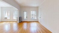 Located on East South Temple Street in Salt Lake City, this 2-bedroom, 1-bathroom unit blends classic architectural character with practical living spaces. Warm hardwood floors flow throughout the main living areas and bedrooms, complemented by crisp white walls and clean crown molding that lend a bright, airy feel to the interior.

The living room is a welcoming space defined by a graceful arched passageway that connects seamlessly to the rest of the unit. Natural light filters in through multiple windows, including a glazed entry door, creating a pleasant and open atmosphere. A traditional cast-iron radiator adds a period-appropriate touch.

The kitchen features white tile flooring, gray lower cabinetry with white upper cabinets, a gas range, and a full-size refrigerator. Built-in shelving and ample storage make it both functional and organized. The kitchen opens toward a carpeted secondary bedroom, which offers built-in upper cabinetry and good natural light.

The primary bedroom features hardwood floors, crown molding, a frosted-glass panel door, and access to a dedicated closet. The bathroom retains its classic charm with a black-and-white hexagonal mosaic tile floor, white subway-tiled walls, a pedestal sink, and a bathtub with shower — a thoughtfully preserved vintage aesthetic throughout.