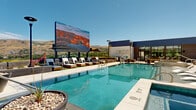 This expansive rooftop amenity deck is a thoughtfully designed outdoor retreat that combines modern architecture with resort-quality amenities. At its center sits a large, crystal-clear swimming pool equipped with in-water sun loungers, accessible pool lift, and an adjacent hot tub framed in stacked stone. A dramatic oversized LED display screen serves as a striking focal point, offering an open-air entertainment experience with panoramic mountain and valley views as a backdrop.

Surrounding the pool, generous deck space is lined with contemporary chaise loungers and shaded pergola-covered cabanas, providing ample areas for relaxation in both sun and shade. Tall outdoor heaters ensure year-round comfort. One side of the deck transitions into a lush turf lawn area with wooden-framed raised planters and additional seating, creating a park-like escape above the city.

The space is anchored by a sleek clubhouse building clad in brick, steel, and floor-to-ceiling glass, featuring a vibrant living green wall that adds a natural, organic element to the modern facade. Decorative concrete planters, sculptural fire features, and carefully curated native landscaping contribute to the polished, cohesive aesthetic. Concrete benches and quiet nooks offer more intimate seating options throughout the deck.