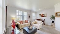 This 1-bedroom, 1-bathroom residence is thoughtfully designed to maximize comfort and functionality across a single floor. The open living room is a welcoming focal point, featuring plush carpeting, crown molding, and multiple large windows dressed with vertical blinds that flood the space with natural light and offer outdoor views. The layout flows seamlessly from the living area into a dedicated dining space, making it ideal for both relaxing and entertaining.

The galley-style kitchen is efficient and well-equipped, featuring white cabinetry with light wood accents, tile flooring, ample counter space, and a full suite of white appliances including a range, microwave, refrigerator, and dishwasher. Abundant upper and lower cabinet storage ensures plenty of room for organization.

The generously sized primary bedroom is a serene retreat, highlighted by a ceiling fan, large windows with views of the outdoors, soft carpet underfoot, and crown molding. A dedicated closet provides excellent storage.

The bathroom is clean and functional, featuring a full tub-shower combination with white tile surround and tile flooring. A hallway connects the rooms, providing a practical and organized flow throughout the residence. Crown molding and a neutral color palette tie the entire space together with a polished, cohesive aesthetic.