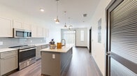 Located at 1710 Belcourt Ave in Nashville, TN, this well-appointed one-bedroom, one-bathroom unit offers a thoughtfully designed single-floor layout. The open-concept living and kitchen area serves as the heart of the space, showcasing rich hardwood-style flooring, clean white walls, and abundant natural light from large windows and a sliding glass door with vertical blinds.

The kitchen is a standout feature, equipped with a central island topped with a white countertop and an undermount sink, complemented by pendant lighting overhead. Two-toned cabinetry — white upper cabinets and gray lower cabinets — pairs with a subway tile backsplash and a full suite of stainless steel appliances, including a refrigerator, range, and microwave.

The bedroom is carpeted for comfort and benefits from natural light through a window with exterior views. The bathroom features gray cabinetry with white countertops and tile flooring, with direct access to a walk-in closet with built-in shelving. Additional storage is provided by two closets, a utility room, and a dedicated laundry area. The overall aesthetic is clean, modern, and functional — ideal for those seeking a contemporary living space in Nashville.