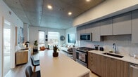 Located in the heart of Portland, Oregon, this contemporary residence at 1510 SW Alder St delivers a refined urban living experience defined by industrial-modern architecture and high-quality finishes throughout. The exposed concrete ceiling is a defining architectural feature, lending a loft-like character to every room while complementing the clean, minimalist aesthetic of the interiors.

The open-concept kitchen and living area form the core of the space. The kitchen is outfitted with flat-front cabinetry in both gray and warm wood tones, a mosaic tile backsplash, stainless steel appliances including a gas range and dishwasher, and a generous island with a white quartz countertop that doubles as a dining and prep surface. Light hardwood flooring runs throughout the main living areas, enhancing the bright, airy atmosphere.

The living room benefits from oversized windows that frame sweeping elevated views of the Portland cityscape and surrounding neighborhoods, filling the space with natural light. The bedroom mirrors this view-oriented design, with large windows overlooking the city and soft carpeting underfoot.

The bathroom features a double-sink vanity with clean white surfaces and a walk-in shower with tiled walls, maintaining the space's modern, polished aesthetic. Throughout, the residence balances industrial elements with warm, livable finishes.
