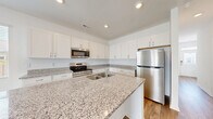 Located at 2108 Silly Soil Ct in Leland, NC, this two-story home offers a thoughtfully designed layout spread across two floors. The main level features an open-concept kitchen and living area anchored by a stunning kitchen with granite countertops, a central island, crisp white shaker cabinets, and stainless steel appliances. Light wood-look flooring runs throughout, complementing the clean, neutral palette. The living room is bright and airy, highlighted by a ceiling fan and sliding glass doors that open to an outdoor view, filling the space with natural light. A garage with an automatic door provides convenient covered parking and additional storage. Upstairs, the primary bedroom is generously sized and bathed in natural light through multiple windows, with a ceiling fan adding comfort. Two additional bedrooms feature large windows with outdoor views and the same warm wood-look flooring. A well-appointed full bathroom with granite vanity, tub-shower combo, and white cabinetry serves the upper level. A dedicated laundry room with wire shelving and washer/dryer hookups adds everyday convenience. The home also includes a hallway closet for extra storage, making it as functional as it is attractive.