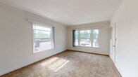 Located at 3053 Stocker Pl in the Leimert Park neighborhood of Los Angeles, this single-floor unit offers a straightforward and functional layout filled with natural light. The living area is generously sized, featuring neutral-toned wall-to-wall carpeting and multiple large windows that allow ample sunlight to stream in, providing views of the surrounding neighborhood. Built-in shelving adds a practical touch to the living space, while a wall-mounted heater and a front entry door with hardware complete the room. An adjacent area showcases warm hardwood flooring, white cabinetry with a built-in countertop and sink, and a window with vertical blinds — ideal for use as a utility or flex space. The bedroom is bright and comfortable, also carpeted, with a large window overlooking the exterior and direct access to the adjoining rooms. The bathroom features a distinctive deep-red diamond-pattern tile floor, a white vanity with mirror, a toilet, and a bathtub, all accented by crisp white walls and a frosted window for privacy. Throughout the unit, a clean, neutral color palette of white walls and light trim creates a cohesive and move-in ready atmosphere well-suited to the Southern California lifestyle.