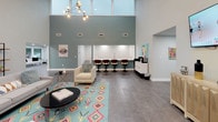 This thoughtfully designed single-floor amenity space combines modern aesthetics with functional versatility. The main lounge is the centerpiece of the space, distinguished by dramatic vaulted ceilings clad in white shiplap and illuminated by a striking sputnik chandelier. Generous large-format gray tile flooring flows throughout, anchored by a vibrant Aztec-patterned area rug that adds a bold pop of color beneath a comfortable seating arrangement of upholstered chairs and a sleek coffee table. A built-in wet bar with a row of tulip-style barstools lines the far wall beneath a double-height teal accent wall, creating a stylish social focal point. Abundant natural light pours in through expansive floor-to-ceiling windows and glass doors that open directly to a pool deck, seamlessly connecting the interior to outdoor amenities. A dedicated co-working or conference nook features a long white-top communal table with modern counter-height chairs, built-in power access, and a window overlooking the pool. A separate intimate dining area offers a round walnut table with casual seating. Throughout the space, vibrant pop-art wall pieces add personality and energy. Recessed lighting and strategically placed pendant fixtures ensure the space is well-lit at all times, creating a welcoming and dynamic environment.