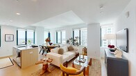 This well-appointed two-bedroom, two-bathroom residence is set on a single level and offers an efficient, thoughtfully designed floor plan bathed in natural light. Large floor-to-ceiling windows frame striking panoramic city skyline views throughout the home, creating a bright and airy atmosphere.

The open-plan kitchen and living area forms the heart of the residence. The kitchen features sleek light wood and white cabinetry, a tile backsplash, stainless steel appliances, and a central island with a built-in sink and generous counter space — ideal for both cooking and casual dining. The adjoining living and dining area benefits from multiple large windows overlooking the cityscape, with light hardwood flooring extending seamlessly throughout.

The primary bedroom is a comfortable retreat, featuring a bold geometric feature wall with warm-toned wallpaper, a round mirror accent, built-in closets, and city views through a large window. The second bedroom continues the high-rise aesthetic with dramatic floor-to-ceiling city views and a striking floral ceiling detail that adds a distinctive design touch.

The two bathrooms are finished in a clean, contemporary style. One features a glass-enclosed walk-in shower with large-format neutral tiles and a wood-toned vanity, while the second offers a full soaking tub with tiled surround and a matching vanity.