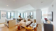 This well-appointed two-bedroom, two-bathroom residence is set on a single level and offers an efficient, thoughtfully designed floor plan bathed in natural light. Large floor-to-ceiling windows frame striking panoramic city skyline views throughout the home, creating a bright and airy atmosphere.

The open-plan kitchen and living area forms the heart of the residence. The kitchen features sleek light wood and white cabinetry, a tile backsplash, stainless steel appliances, and a central island with a built-in sink and generous counter space — ideal for both cooking and casual dining. The adjoining living and dining area benefits from multiple large windows overlooking the cityscape, with light hardwood flooring extending seamlessly throughout.

The primary bedroom is a comfortable retreat, featuring a bold geometric feature wall with warm-toned wallpaper, a round mirror accent, built-in closets, and city views through a large window. The second bedroom continues the high-rise aesthetic with dramatic floor-to-ceiling city views and a striking floral ceiling detail that adds a distinctive design touch.

The two bathrooms are finished in a clean, contemporary style. One features a glass-enclosed walk-in shower with large-format neutral tiles and a wood-toned vanity, while the second offers a full soaking tub with tiled surround and a matching vanity.