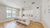 Located at 147 Pinewind Way in Goose Creek, South Carolina, this single-floor space offers a clean, modern aesthetic defined by crisp white finishes, light hardwood flooring, and an abundance of natural light. The layout comprises two distinct areas that together create a cohesive and functional environment.

The kitchen is a standout feature, designed with bright white shaker-style cabinetry, white subway tile backsplash, and sleek quartz countertops. A generous central island anchors the space and provides seating for multiple guests via stylish wood-and-metal bar stools. A stainless steel undermount sink, recessed lighting, and globe pendant lights suspended from the ceiling add refined detail. Large windows frame views of the outdoor surroundings, flooding the kitchen with natural daylight and enhancing the open, airy feel.

The office area is equally well-appointed, featuring large double-hung windows with transom panels that draw in generous amounts of natural light. Crown molding adds a polished architectural touch, while the neutral wall tones create a calm, focused atmosphere. The space accommodates a full workstation setup and additional storage furnishings with ease.

Throughout, the light hardwood floors, white trim, and soft neutral palette contribute to a bright, welcoming ambiance that is both practical and visually appealing.