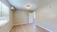 Located at 200 Robert Stroae in New Smyrna Beach, Florida, this single-floor space offers a thoughtfully updated interior with a cohesive, neutral design scheme. Light wood-look flooring runs throughout, lending warmth and continuity to each room.

The living area is open and airy, featuring a ceiling fan with light fixture and a textured ceiling. Warm beige-toned walls create a welcoming atmosphere, and the space flows naturally toward the kitchen and other areas of the unit.

The kitchen stands out with crisp white cabinetry, stone-look quartz countertops with subtle veining, a black electric range, and an overhead exhaust hood. The clean contrast between the white cabinetry and black appliances gives the kitchen a modern, functional feel.

The bedrooms are well-proportioned and bright, each featuring the same light flooring, textured ceilings, and neutral wall tones. One bedroom includes a wall-mounted mini-split air conditioning unit for individualized climate control, while another benefits from a ceiling fan and a window that allows natural light to filter in.

The bathroom is straightforward and functional, featuring a full tub-shower combination with a white surround, a toilet, and a vanity with sink, all finished with coordinating hardware. The consistent wood-look flooring extends into the bathroom as well, maintaining visual unity across the space.