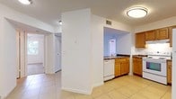 This single-floor residence offers a practical and comfortable layout across several distinct living areas. The kitchen is well-equipped with warm honey-toned wood cabinetry, dark granite-style countertops, white appliances including a refrigerator, electric range, dishwasher, and a sink positioned beneath a pass-through opening that connects to the main living area. Light ceramic tile flooring runs throughout the kitchen and extends into the living spaces, providing a clean and cohesive look. The living room is bright and open, benefiting from natural light that pours in through a large sliding glass door fitted with vertical blinds, offering access to an outdoor area and views of surrounding greenery. The bedrooms are finished with plush carpeting and each features a ceiling fan with lighting, along with windows dressed in vertical blinds that allow natural light. The bathroom includes tile flooring, a vanity with wood cabinetry, a toilet, and a shower-tub combination. Throughout the residence, textured ceilings and crisp white walls create a clean, neutral backdrop. Closet space is visible in the hallway area, adding practical storage. The overall layout is efficient and well-connected, making the space comfortable and easy to navigate.