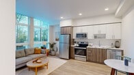 Located at 1670 SW Alder St in Portland, Oregon, this efficiently designed studio presents a thoughtfully organized open-plan layout that seamlessly integrates the kitchen and living area into a single cohesive space. Light hardwood flooring runs throughout, lending warmth and visual continuity to every corner.

The kitchen is well-appointed with a full suite of stainless steel appliances, including a refrigerator, electric range, built-in microwave, and dishwasher. Cabinetry combines crisp white upper cabinets with wood-toned lower cabinets, complemented by clean light countertops and a single-basin sink. A small dining nook adjacent to the kitchen accommodates an intimate round table, making efficient use of the available footprint.

The living area is the standout of the space, anchored by dramatic floor-to-ceiling windows that flood the interior with abundant natural light and offer views of the surrounding greenery. The airy, open ambiance created by these windows gives the space a sense of openness well beyond its physical footprint. Recessed lighting in the kitchen and clean white walls throughout further enhance the bright, modern aesthetic.

The overall design reflects a contemporary urban sensibility — practical, clean-lined, and light-filled — making it a well-suited residence in the heart of Portland's vibrant west side.