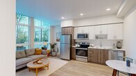 Located at 1670 SW Alder St in Portland, Oregon, this efficiently designed studio presents a thoughtfully organized open-plan layout that seamlessly integrates the kitchen and living area into a single cohesive space. Light hardwood flooring runs throughout, lending warmth and visual continuity to every corner.

The kitchen is well-appointed with a full suite of stainless steel appliances, including a refrigerator, electric range, built-in microwave, and dishwasher. Cabinetry combines crisp white upper cabinets with wood-toned lower cabinets, complemented by clean light countertops and a single-basin sink. A small dining nook adjacent to the kitchen accommodates an intimate round table, making efficient use of the available footprint.

The living area is the standout of the space, anchored by dramatic floor-to-ceiling windows that flood the interior with abundant natural light and offer views of the surrounding greenery. The airy, open ambiance created by these windows gives the space a sense of openness well beyond its physical footprint. Recessed lighting in the kitchen and clean white walls throughout further enhance the bright, modern aesthetic.

The overall design reflects a contemporary urban sensibility — practical, clean-lined, and light-filled — making it a well-suited residence in the heart of Portland's vibrant west side.