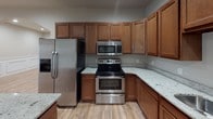 This single-floor residence offers a thoughtfully designed layout with a cohesive neutral color palette and light wood-look flooring throughout the main living areas. The kitchen is a functional centerpiece, featuring warm medium-toned wood cabinetry, light granite countertops, stainless steel appliances including a French door refrigerator and dishwasher, and a stainless undermount sink — all illuminated by recessed lighting. An elegant arched passageway connects the kitchen to the open living and dining areas, which are distinguished by classic raised-panel wainscoting, adding architectural character to the space. A sliding glass door in the living area provides access to the outdoors and fills the room with natural light. Multiple versatile rooms offer flexibility for use as bedrooms or additional living spaces, each finished with recessed lighting and neutral walls. The dedicated laundry room houses a full-size washer and dryer alongside utility systems, with tile flooring for easy maintenance. The bathrooms are finished with large-format tile surrounds, glass sliding tub-shower enclosures, and dark-toned vanities with stone countertops. The overall design balances practical functionality with clean, modern finishes throughout.
