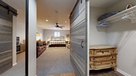This thoughtfully designed single-floor retreat offers a seamless blend of rustic character and contemporary comfort. The generously sized bedroom serves as the heart of the space, anchored by a classic iron-frame bed set against a striking shiplap accent wall. Recessed lighting and a ceiling fan overhead provide both function and ambiance, while soft, neutral carpeting underfoot adds warmth throughout. The bedroom doubles as a comfortable living area, with ample room for a full sofa seating arrangement and additional accent chairs, making it ideal for relaxing in style.

A standout architectural feature is the reclaimed wood sliding barn door, which adds a distinctive farmhouse aesthetic and separates the main living space from the entry corridor. The hallway, finished with smooth flooring, leads to the front entrance and provides access to the closet and bathroom. Wall art, including a bold black-and-white equine portrait, reinforces the rustic theme carried throughout the space.

The bathroom is clean and functional, featuring a full tub-shower combination with classic white tile surround. A dedicated closet with open shelving offers convenient storage. Natural light filters in through a window in the bedroom, complementing the recessed lighting to keep the space feeling bright and welcoming. Overall, this retreat exudes a cozy, cabin-inspired atmosphere with purposeful design details at every turn.