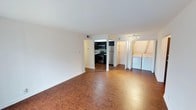 This single-floor residence offers a thoughtfully designed layout that balances functionality and comfort. The open living area is anchored by rich, warm hardwood-style flooring that extends throughout the main living spaces, with large sliding glass doors dressed in vertical blinds that invite abundant natural light and provide access to the outdoors. A dedicated entry door adds a sense of arrival and privacy.

The kitchen is outfitted with dark espresso cabinetry, light stone-look countertops, and a full suite of stainless steel appliances including a gas range, over-the-range microwave, refrigerator, and dishwasher — offering a sleek, modern aesthetic ideal for everyday cooking.

Conveniently located off the main living area is an in-unit laundry alcove with a full-size washer and dryer, adding practical value to the home. The bedroom features plush wall-to-wall carpeting, a bright window with blinds for natural light and privacy, and a spacious closet with mirrored sliding doors and built-in shelving and hanging rods, providing generous storage.

The bathroom is finished with large-format gray tile surrounding a full soaking tub and shower combination, complemented by chrome fixtures for a clean, contemporary look. Clean white walls and neutral tones throughout the space create a bright, cohesive ambiance.