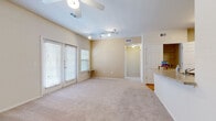 This single-floor residence offers a thoughtfully arranged layout with a comfortable, functional design throughout. The living area is generously sized, featuring soft neutral carpet, warm beige walls, and vaulted ceilings equipped with both a ceiling fan and track lighting. Large windows with horizontal blinds and a set of French doors allow abundant natural light to fill the space while providing outdoor access. A pass-through counter connects the living area to the kitchen, enhancing the open feel of the floor plan. The kitchen is well-appointed with warm honey-toned wood cabinetry, granite-style countertops, and white appliances including a refrigerator, electric range, and over-the-range microwave. Light hardwood flooring runs through the kitchen and connects seamlessly to adjacent spaces. A spacious walk-in closet is conveniently located just off the kitchen area, providing ample storage. The bedroom is carpeted and bright, featuring a ceiling fan and a pair of windows that invite natural light and outdoor views. The bathroom showcases hardwood flooring, warm wood vanity cabinetry, a white countertop with integrated sink, a large mirror, and a glass-enclosed shower, creating a clean and inviting atmosphere throughout.