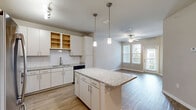 Located at 180 Woodruff Rd in Greenville, SC, this well-appointed one-bedroom, one-bathroom residence offers a thoughtfully designed single-level layout. The open-concept kitchen and living area serves as the heart of the home, where light wood-look flooring flows throughout. The kitchen is outfitted with crisp white cabinetry, a classic subway tile backsplash, gleaming granite countertops, a large center island with pendant lighting overhead, and a full suite of stainless steel appliances including a refrigerator, range, microwave, and dishwasher. Track lighting adds a modern touch to the space. The living area benefits from natural light provided by multiple windows and a sliding glass door, complemented by a ceiling fan. The generously sized primary bedroom features soft carpeting, a ceiling fan, and a dedicated walk-in closet. The bathroom is a refined retreat, complete with wood-look tile flooring, a granite-topped vanity, built-in shelving, and a frameless glass walk-in shower adorned with elegant marble-style tile. Neutral wall tones and clean white trim throughout create a cohesive, move-in-ready aesthetic.
