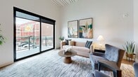 Located at 201 Grand Blvd in the heart of Kansas City, MO, this well-appointed one-bedroom, one-bathroom residence offers a thoughtfully designed layout with modern finishes throughout. The open-concept kitchen and living area serves as the centerpiece of the home, featuring striking dark-toned cabinetry that extends to the ceiling, stainless steel appliances, a white subway tile backsplash, and a kitchen island with bar seating — all set atop warm wood-tone flooring. The living room impresses with soaring ceilings accented by a decorative paneled detail, large floor-to-ceiling sliding glass doors that flood the space with natural light, and direct access to a private balcony overlooking the Kansas City skyline and Grand Boulevard streetscape. The carpeted bedroom is a comfortable retreat with a ceiling fan, a large window framing neighborhood views, and access to a dedicated closet. The full bathroom is finished with large-format gray tile flooring, sleek gray cabinetry, a wide vanity with a white countertop, a full-width mirror, and a tiled shower-tub combination. Clean white walls, black window framing, and contemporary hardware tie the design together, creating a cohesive and modern urban living experience.