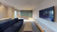 Located at 333 S Glebe Rd in Arlington, Virginia, this single-floor amenity space is thoughtfully designed with a cohesive contemporary aesthetic that blends bold color accents with refined materials. The welcoming lobby serves as a striking introduction, anchored by a sculptural gold multi-bulb chandelier suspended above a seating arrangement featuring a tufted gray sofa, teal accent chairs, and a marble-topped coffee table. A decorative geometric lattice screen wall and rich wood-paneled walls frame the space, while terrazzo flooring adds a polished, durable foundation.

Adjacent lounge and gathering areas continue the design language, incorporating patterned carpeting, a tufted navy sofa, large-format television, and built-in media cabinetry. A bold teal-and-gold geometric accent wall anchors the dining zone, which includes a communal table with seating for multiple guests.

The catering kitchen is outfitted with warm wood cabinetry, expansive marble-look quartz countertops, a white subway tile backsplash, and geometric gold pendant lighting. A separate conference or meeting room features floor-to-ceiling teal upholstered acoustic panels, a wood-slat ceiling, a central conference table, and a wall-mounted display screen—ideal for private gatherings or presentations. Natural light filters through windows in several areas, enhancing the overall bright and welcoming ambiance.