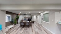 This single-floor leasing office in Phoenix, Arizona, is designed to offer a professional yet approachable environment for prospective residents. The space is finished with light wood-look luxury vinyl plank flooring throughout, contributing to a clean, contemporary aesthetic that flows seamlessly across all areas.

The main reception area serves as the focal point of the office, anchored by a substantial dark wood-toned desk equipped with a workstation and upper cabinetry for storage. A counter-height bar along one wall, paired with wooden stools, provides an additional area for informal consultations or paperwork. Recessed lighting illuminates the space evenly, complemented by ceiling fans that enhance comfort.

A dedicated lounge area features a mounted flat-screen television set against a gray tile accent wall, alongside a navy blue seating arrangement and lush indoor plants, creating a relaxed atmosphere for waiting guests. An intimate meeting nook with a round bistro table and vibrant blue chairs offers views of the surrounding community through windows fitted with blinds.

The neutral gray color palette, accented by warm wood tones and pops of color, gives the office a balanced, inviting character. Multiple private rooms branch off a central hallway, ensuring that confidential leasing conversations can be conducted comfortably.