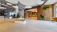 Located at 107 Wardlaw St in Greenville, South Carolina, this single-floor lobby and amenity space presents a striking blend of industrial and contemporary design. The expansive open-plan layout is anchored by polished light-toned tile flooring and soaring ceilings with exposed ductwork, steel-framed columns, and striking circular acoustic panels that contribute to both the aesthetic and acoustic quality of the space.

The main lounge area is bathed in abundant natural light streaming through floor-to-ceiling windows, offering views of the surrounding Greenville streetscape. Curated seating arrangements — featuring leather sofas, velvet accent chairs in deep blue with gold frames, and a vivid teal watercolor-inspired area rug — create an inviting and artful atmosphere. Statement pendants with Edison-style bulbs and a dramatic large-scale painting add to the gallery-like character of the space.

Integrated throughout the lobby are lush planters and potted tropical greenery, bringing warmth and a biophilic quality to the industrial setting. A dedicated mail room, finished with warm gray textured walls, gold trim accents, a globe chandelier, and framed artwork, provides a refined and functional amenity. A slatted wood accent wall with moss art installations further enhances the lobby's distinctive, design-forward identity.