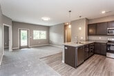 This single-floor residence is designed with a contemporary, open-concept layout that promotes a seamless flow between living and kitchen spaces. The kitchen is a standout feature, outfitted with dark espresso cabinetry, granite-style countertops, and a full suite of stainless steel appliances, including a range, microwave, and refrigerator. A peninsula with a double stainless steel sink and pendant lighting above serves as both a functional workspace and a natural divider between the kitchen and the adjacent living area, which features wood-look flooring and plush carpeting.

The bedrooms are carpeted and bathed in natural light from multiple windows with outdoor views of surrounding greenery. The primary bedroom is generously proportioned, offering direct access to an en-suite bathroom and a walk-in closet equipped with wire shelving and hanging systems on multiple walls. The bathrooms feature the same dark cabinetry and granite-style countertops found in the kitchen, with wood-look flooring and a tub-shower combination. Neutral warm-gray tones are carried consistently throughout, lending the space a cohesive, modern aesthetic.