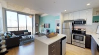 This contemporary high-rise unit is designed with a clean, modern aesthetic that seamlessly blends function and style across a single floor. The open-concept kitchen is a standout feature, showcasing two-tone cabinetry with dark wood lower cabinets and crisp white uppers, a large center island with a white quartz countertop, stainless steel appliances, and light hardwood flooring. A vibrant teal accent wall adds a pop of color that ties the kitchen into the adjoining living area.

The living room is bright and inviting, anchored by floor-to-ceiling windows and sliding glass doors that open to a balcony, offering sweeping panoramic city and mountain views. An exposed concrete ceiling lends an industrial character, while a statement pendant light adds warmth to the space.

The bedrooms are thoughtfully designed, each featuring large windows that frame expansive cityscape vistas, carpeted flooring, and ample closet space. One bedroom includes a built-in desk area with a full-length mirror, ideal for a study or workspace.

The bathroom maintains the unit's modern sensibility with dark tile flooring, a wood-finish vanity, and clean white walls. Throughout the space, recessed lighting, neutral tones, and quality finishes create a cohesive and polished urban living environment.