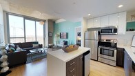 This contemporary high-rise unit is designed with a clean, modern aesthetic that seamlessly blends function and style across a single floor. The open-concept kitchen is a standout feature, showcasing two-tone cabinetry with dark wood lower cabinets and crisp white uppers, a large center island with a white quartz countertop, stainless steel appliances, and light hardwood flooring. A vibrant teal accent wall adds a pop of color that ties the kitchen into the adjoining living area.

The living room is bright and inviting, anchored by floor-to-ceiling windows and sliding glass doors that open to a balcony, offering sweeping panoramic city and mountain views. An exposed concrete ceiling lends an industrial character, while a statement pendant light adds warmth to the space.

The bedrooms are thoughtfully designed, each featuring large windows that frame expansive cityscape vistas, carpeted flooring, and ample closet space. One bedroom includes a built-in desk area with a full-length mirror, ideal for a study or workspace.

The bathroom maintains the unit's modern sensibility with dark tile flooring, a wood-finish vanity, and clean white walls. Throughout the space, recessed lighting, neutral tones, and quality finishes create a cohesive and polished urban living environment.